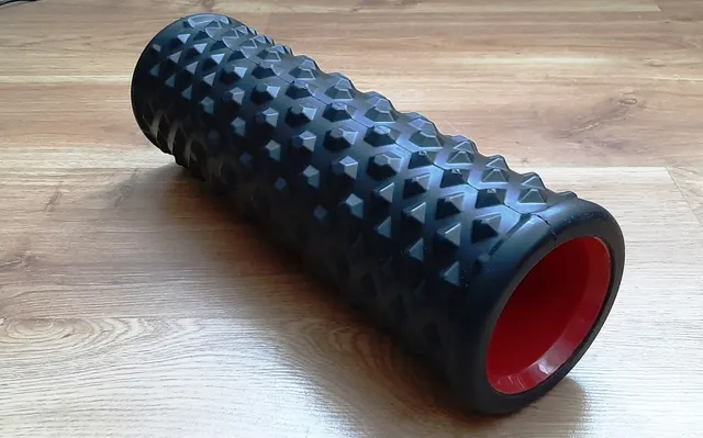 Un rouleau de massage noir texturé, à cœur creux, posé sur un parquet